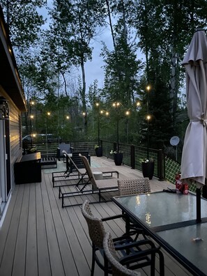 Une terrasse extérieure avec un plancher en bois, une table à plateau en verre et plusieurs chaises.