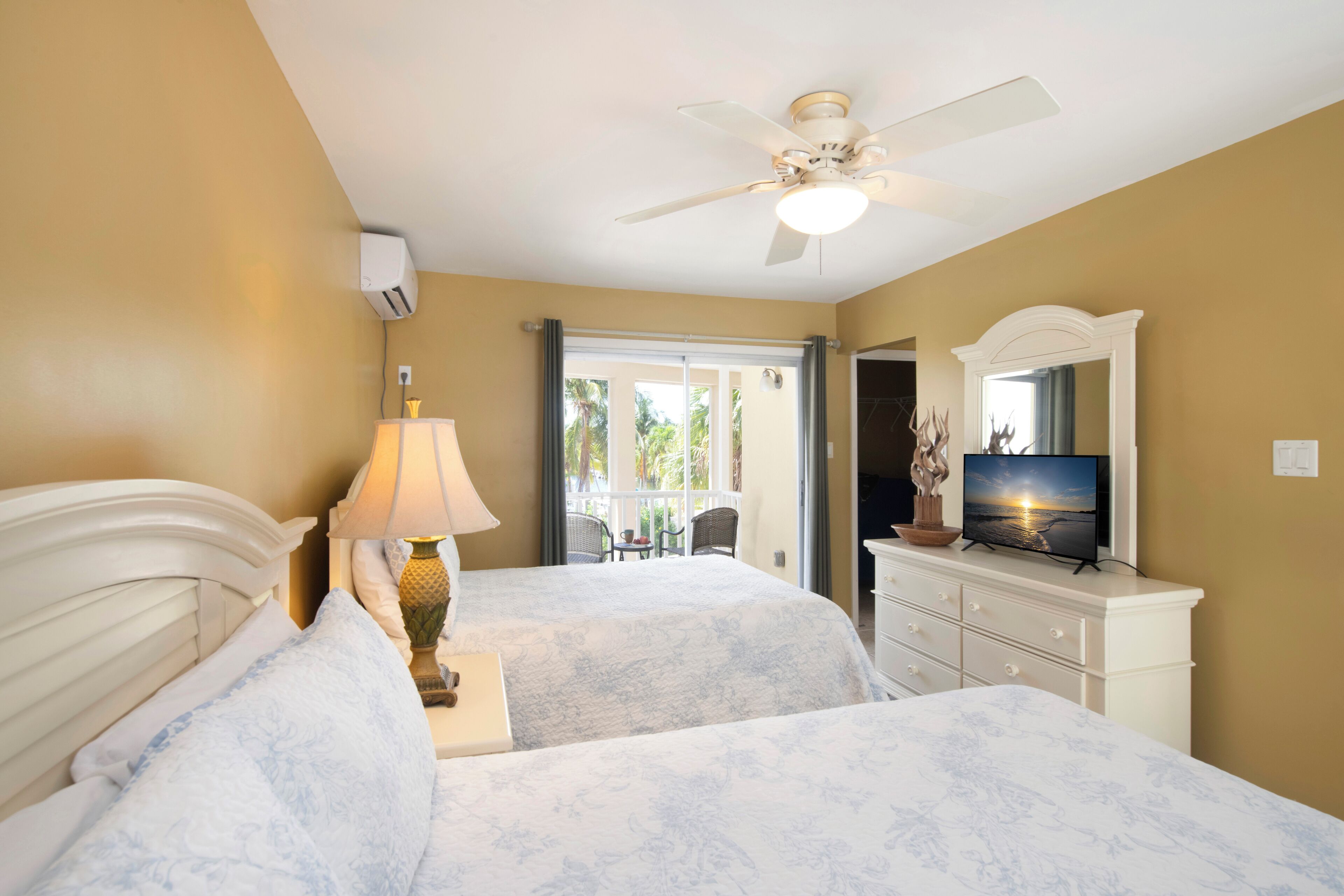 A hotel room with two beds, a ceiling fan, a television, and a view of the outdoors.