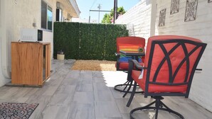 A patio with two red chairs, a small table, and a wooden cabinet with a microwave. - West Racquet Club Art Hall (Palm Springs)