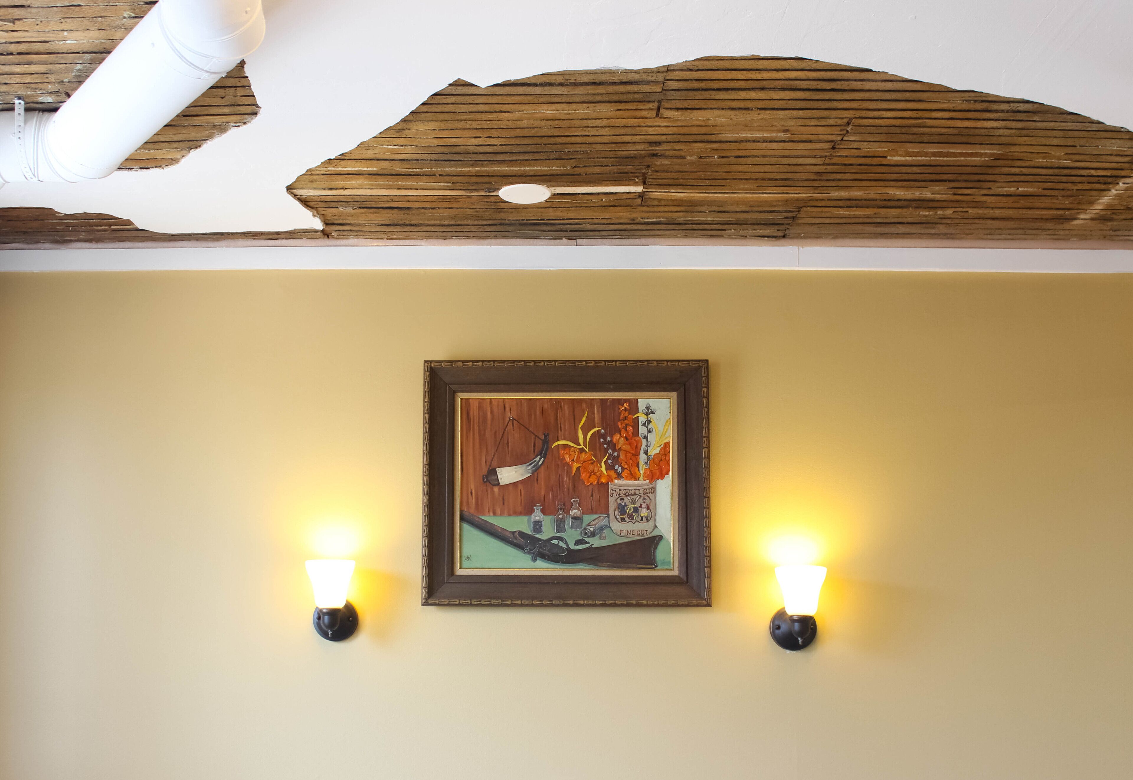 A framed artwork on a wall with two wall-mounted lights on either side.