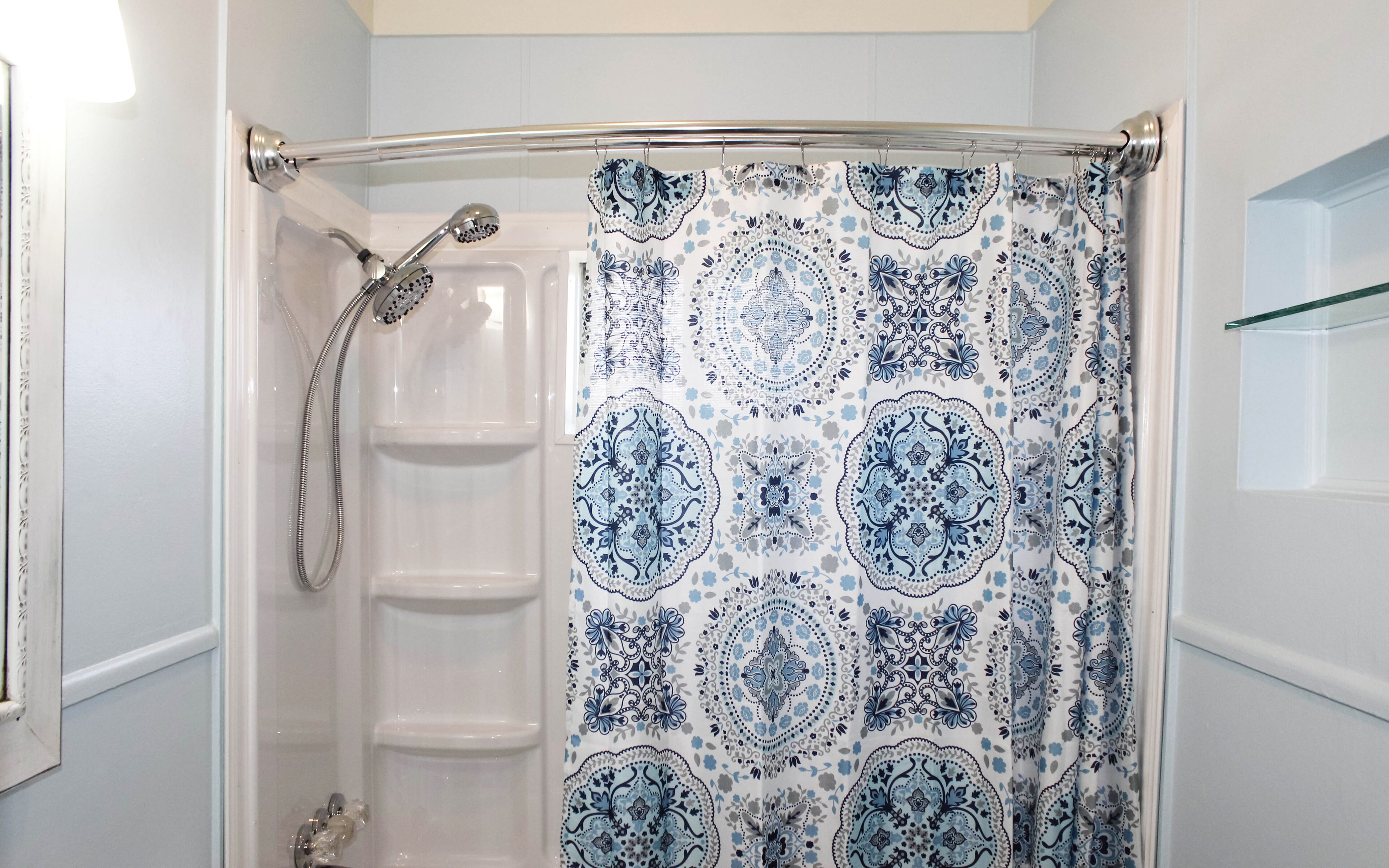 A bathroom with a shower curtain featuring a blue and white pattern, a glass shower enclosure, and a glass shelf to the right.