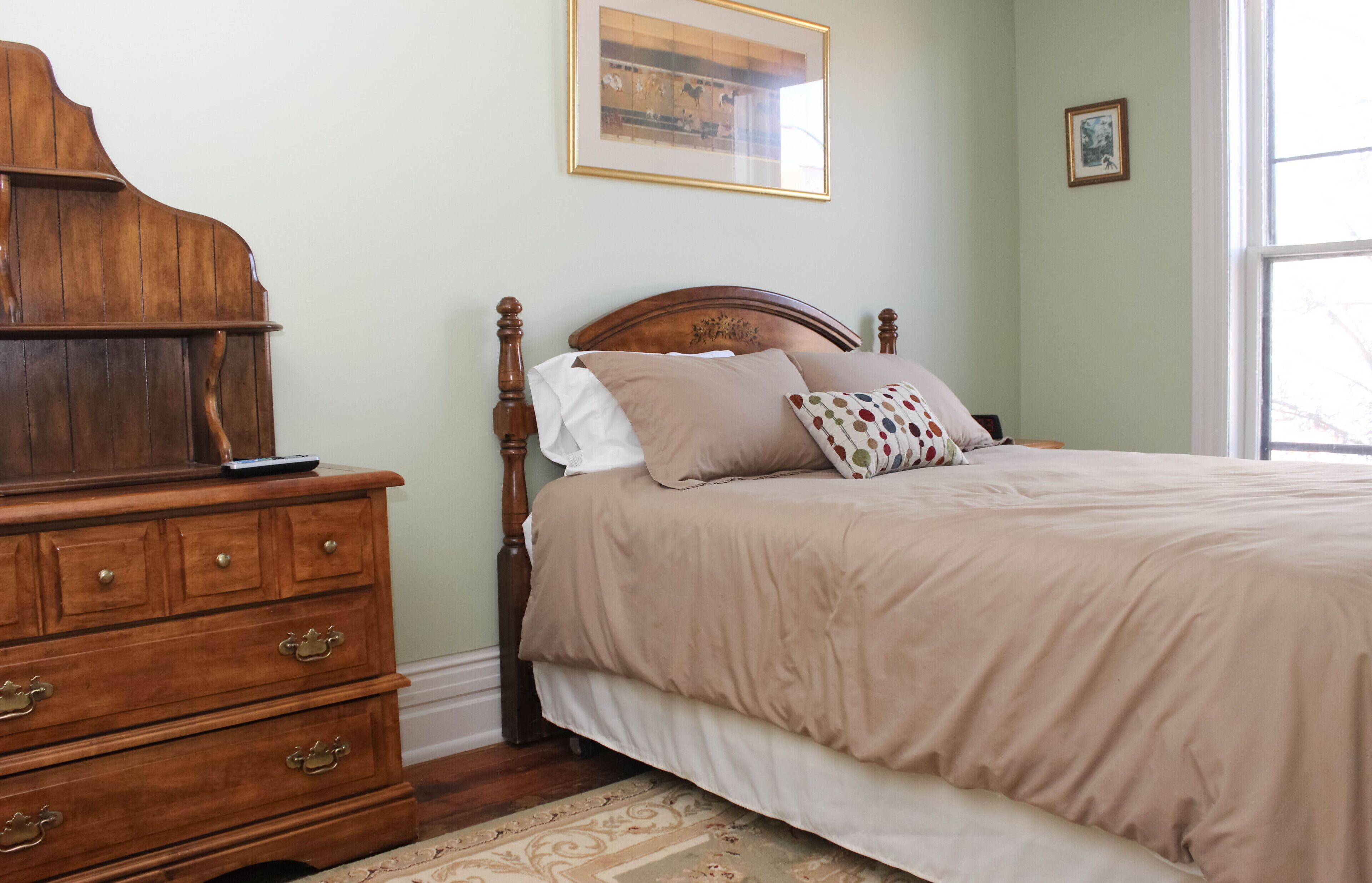 Un dormitorio con un aparador de madera, una cama con colcha color beige y un cuadro enmarcado en la pared.