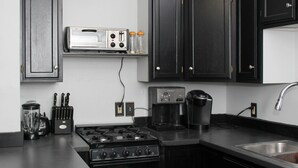 Cozinha com armários escuros, fogão, cafeteira e torradeira.
