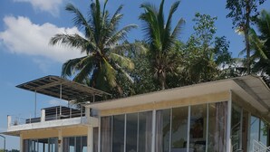 Un edificio moderno de dos pisos con balcón, ventanas amplias y un patio con mobiliario exterior.
