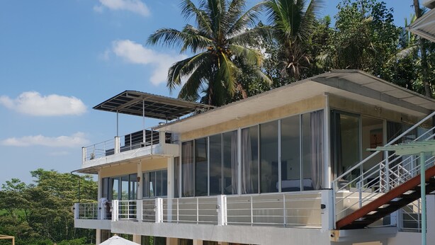 Un edificio moderno de dos pisos con piscina, mobiliario exterior y una escalera que conduce a un balcón.