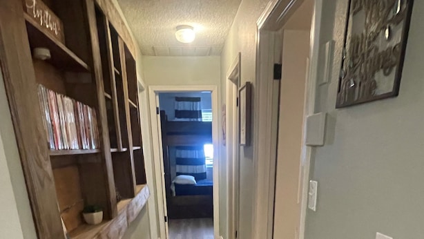 Un pasillo estrecho con piso de madera, una estantería y una puerta que da a un dormitorio.