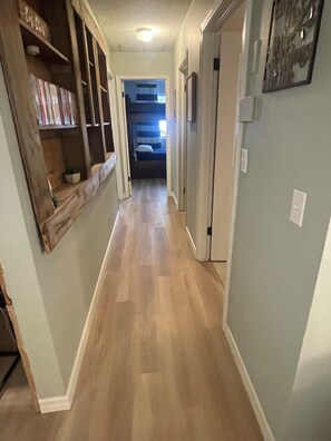 Un pasillo estrecho con piso de madera, una estantería y una puerta que da a un dormitorio.