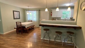 Un comedor con una mesa y sillas de madera, una cocina con ventana y una barra con taburetes.