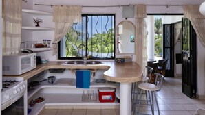 A compact kitchen with a microwave, stove, sink, and bar stools.