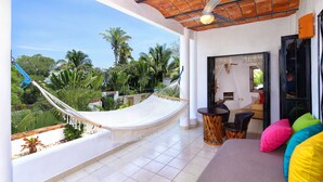 A balcony with a hammock, a sofa with colorful cushions, and a view of palm trees.