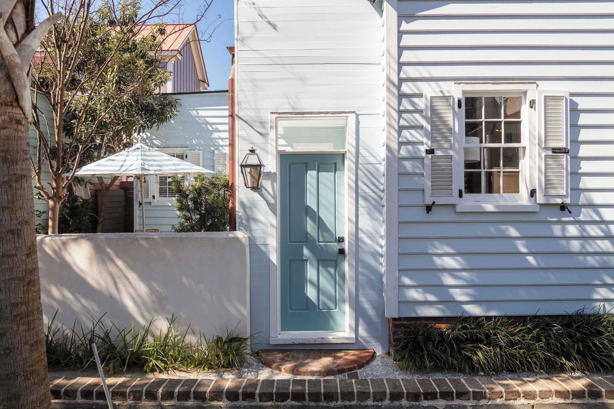 A white house with a teal door, a small porch, and a window with shutters.