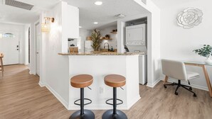Cocina moderna con barra, dos taburetes, una mesa de comedor con una silla y un elemento decorativo en la pared.