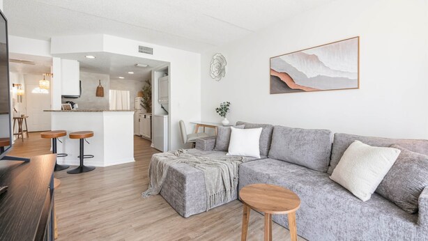 Un salón moderno con un sofá gris, una mesa de centro de madera y una cocina al fondo.