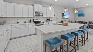 Una cocina moderna con armarios blancos, una isla grande con taburetes y lámparas colgantes.
