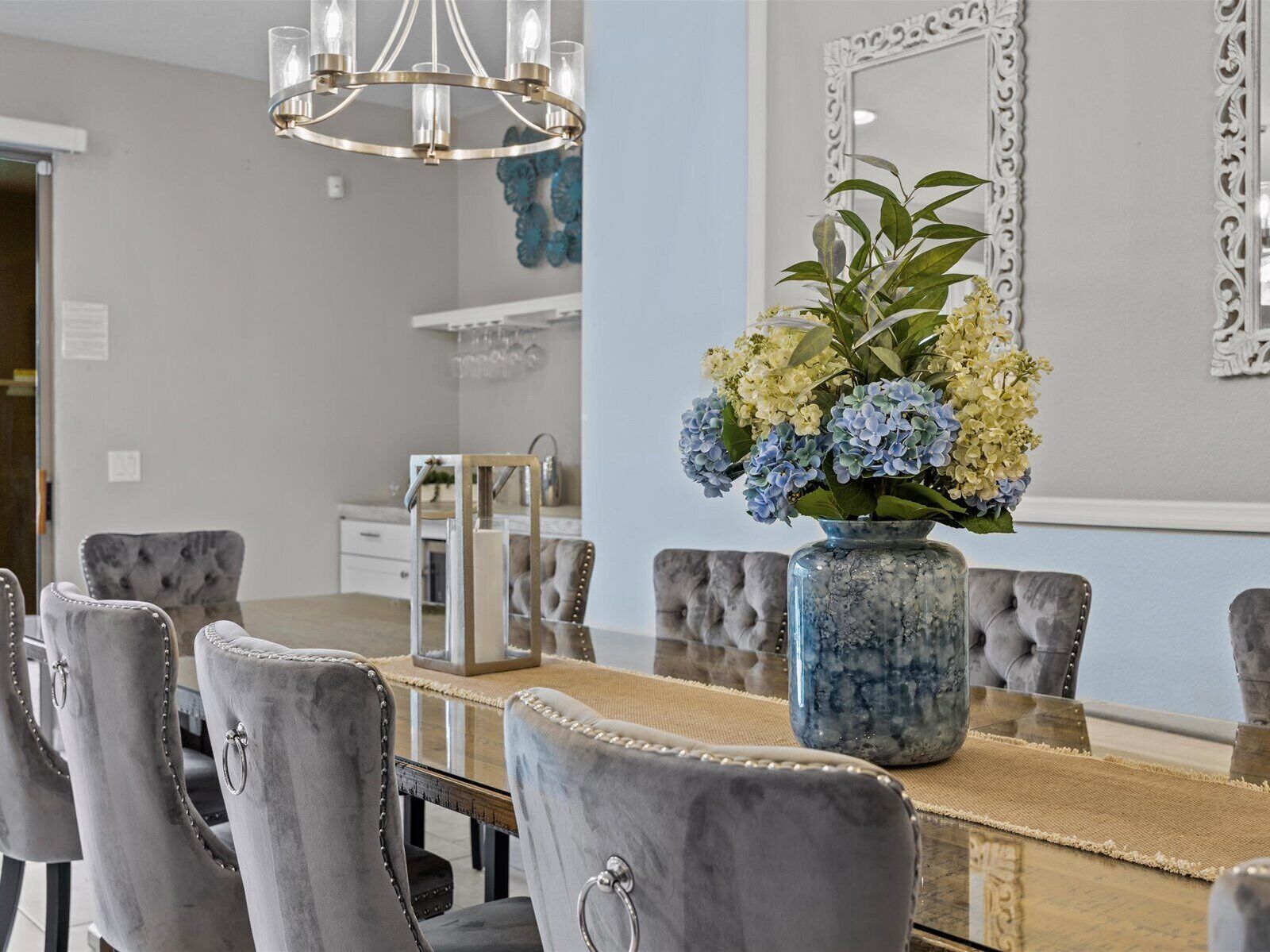 A dining area with a marble-top table, grey upholstered chairs, a vase with flowers, and a chandelier.