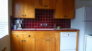 A kitchen with wooden cabinets, a white dishwasher, and a red and white checkered floor.