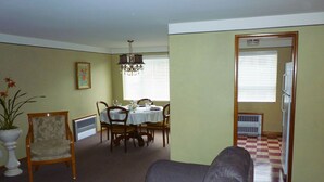 A living room with a gray sofa, dining table set with chairs, a chandelier, and a potted plant.