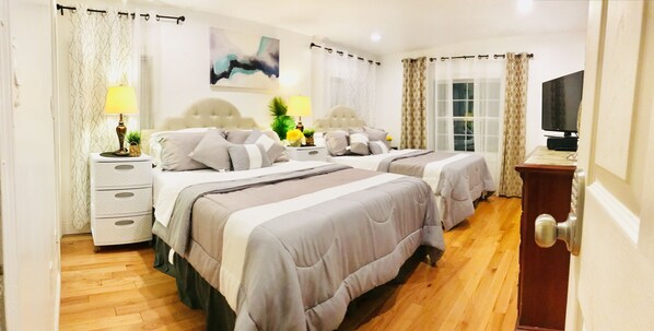 A hotel room with two beds, a TV, a nightstand, a lamp, and a window with curtains.