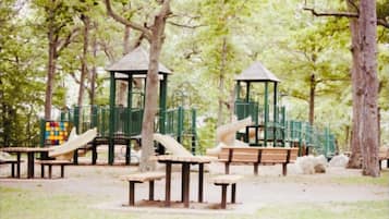 Ein Spielplatz mit Rutschen, Schaukeln und Picknicktischen in einem Park.