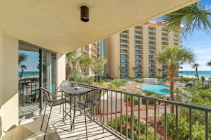 A balcony with a table and chairs, overlooking a pool and a high-rise building. - Million Dollar View On Family Friendly Beach - Includes Beach Chairs  (Panama City Beach)
