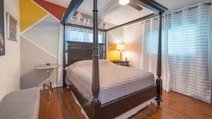 Ein Zimmer mit einem Himmelbett, einer kleinen, runden Tisch und einem Fenster mit Vorhängen, das eine geneigte Decke hat.