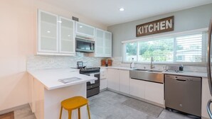 Eine moderne Küche mit weißen Schränken, einem Edelstahlkühlschrank und einem großen Fenster, das für natürliches Licht sorgt.