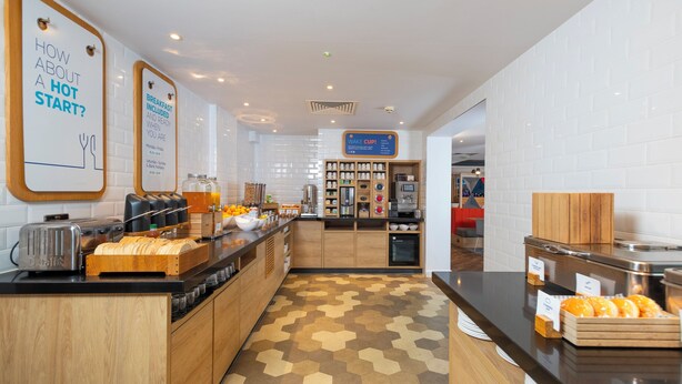 A modern breakfast area with a counter displaying pastries and a sign indicating breakfast is included. - Holiday Inn Express Exeter - City Centre by IHG (Exeter)