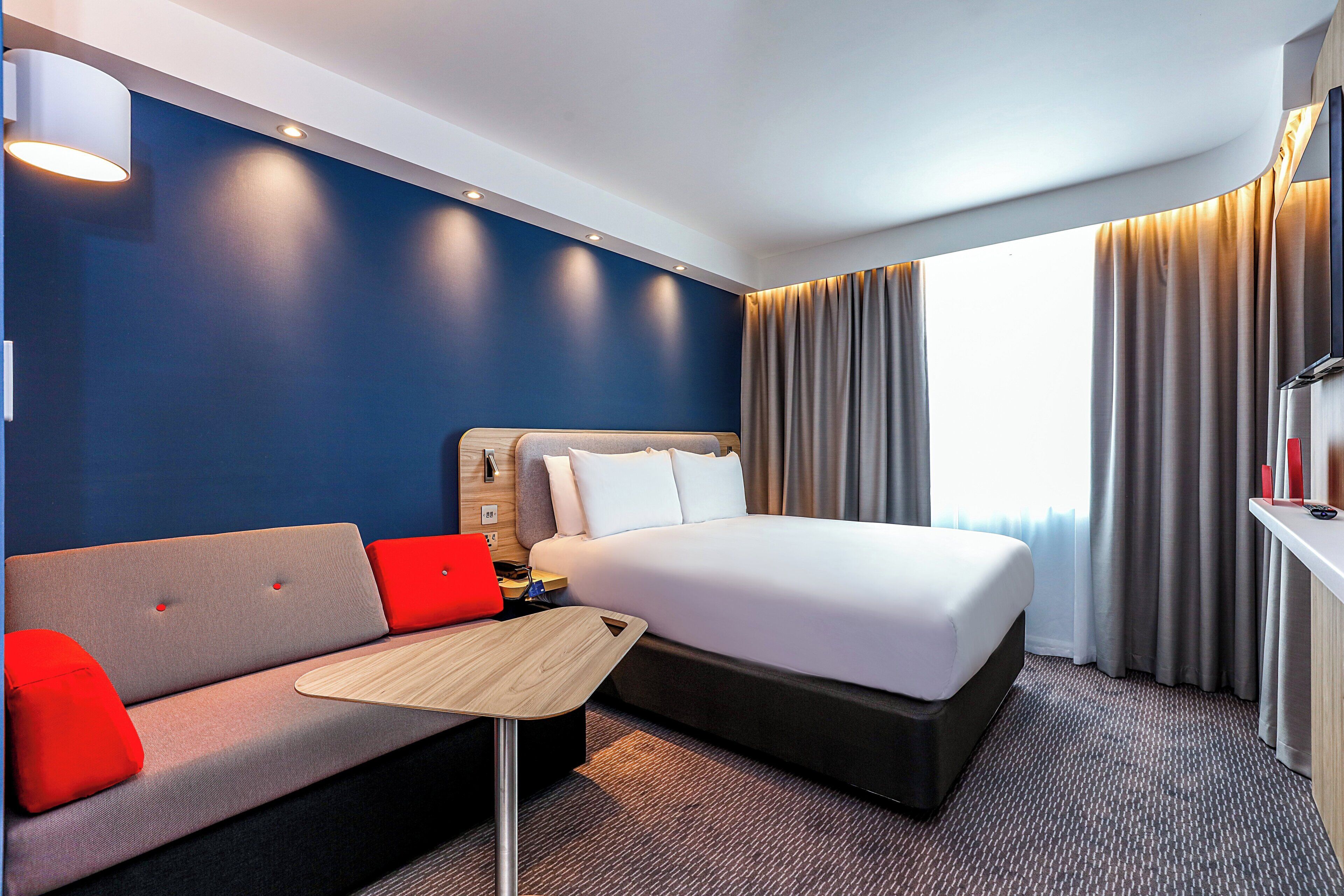A hotel room with a bed, a sofa, a small table, and a TV.