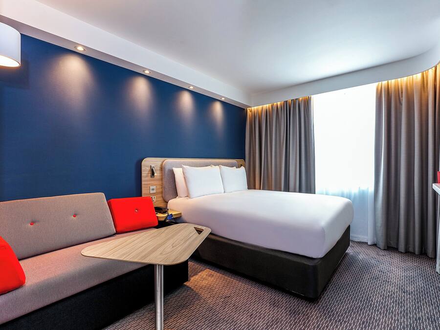 A hotel room with a bed, a sofa, a small table, and a TV.