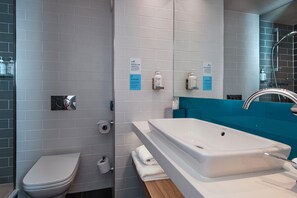 A modern bathroom with a toilet, sink, and shower. There are signs on the wall and toiletries on shelves.