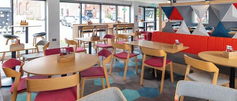 Interior moderno de restaurante con mesas y sillas redondas, un banco con cojín rojo y amplios ventanales con vista a la calle.