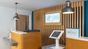 A Holiday Inn Express reception desk with a wooden panel wall, a digital kiosk, and pendant lighting. - Holiday Inn Express Exeter - City Centre by IHG (Exeter)
