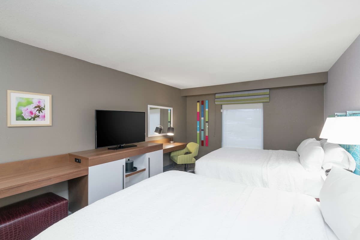 A hotel room with two beds, a desk with a TV, a chair, and a window with blinds.