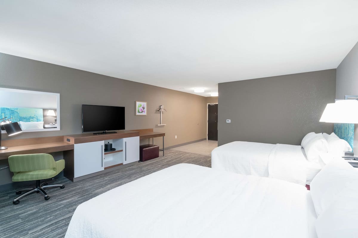 A hotel room with two beds, a desk with a television, a chair, and a lamp.