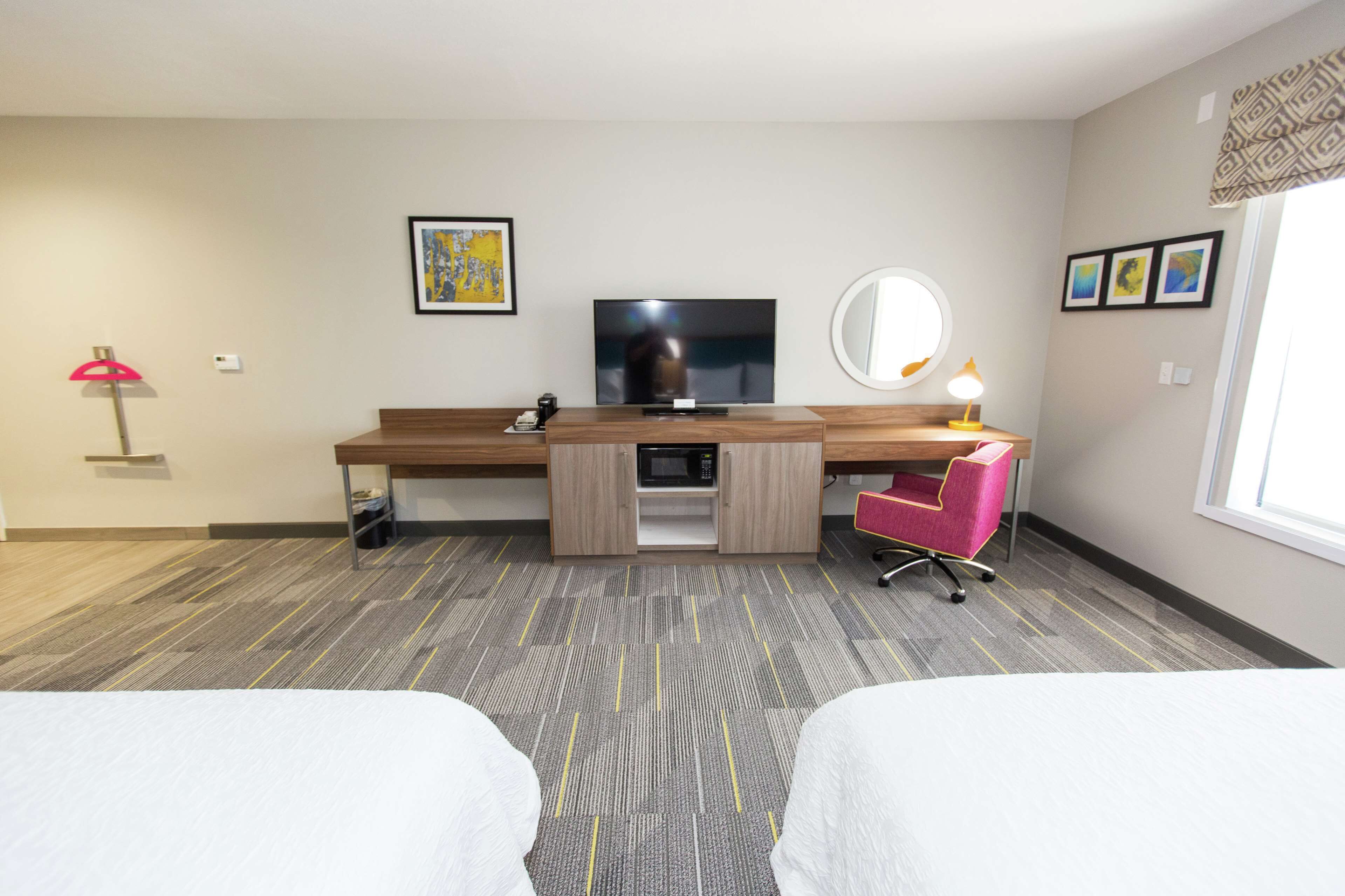 A hotel room with a bed, a desk with a computer, a TV, a microwave, a chair, and a window.