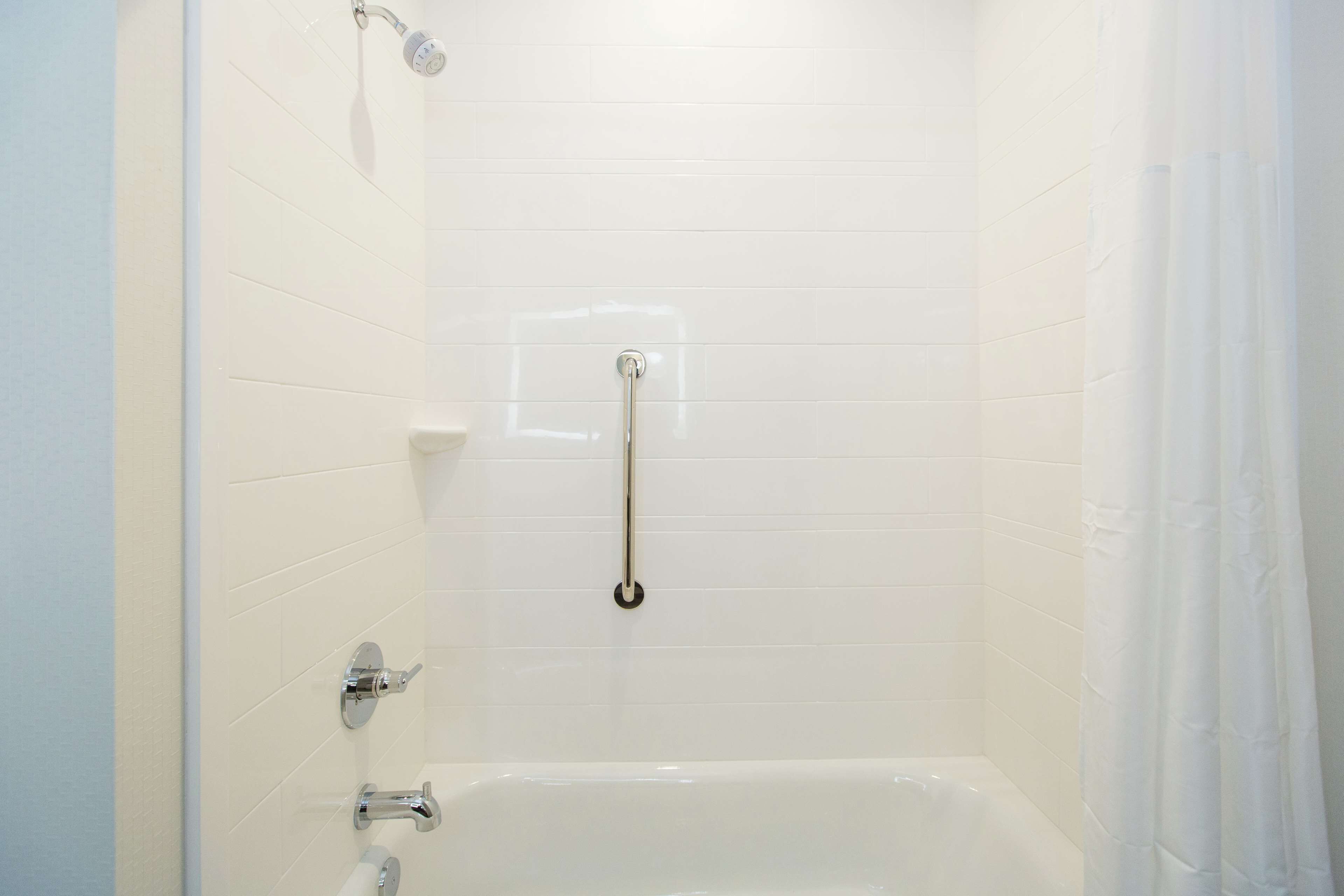 A white-tiled shower with a handheld showerhead, a handheld shower bar, and a handheld faucet.