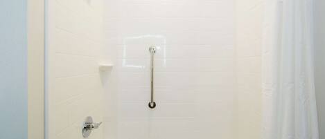 A white-tiled shower with a handheld showerhead, a handheld shower bar, and a handheld faucet.