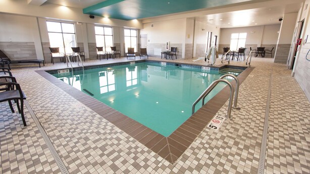 Una piscina con suelo de baldosas y sillas alrededor.