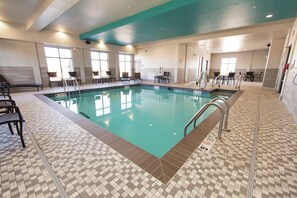 A swimming pool with tiled flooring and chairs around the perimeter.