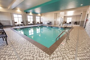 A swimming pool with tiled flooring and chairs around the perimeter.