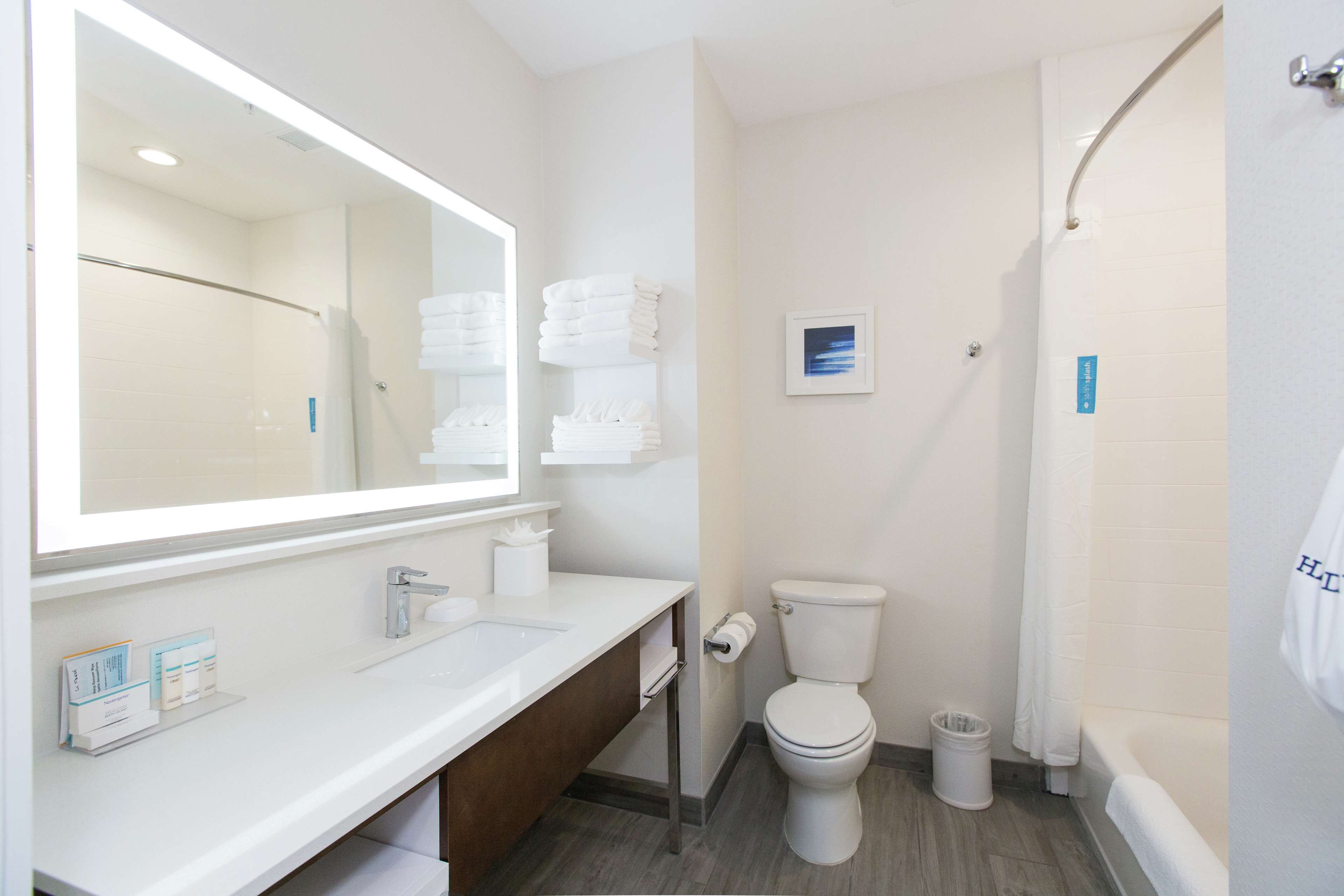Un baño moderno con un espejo grande, sanitarios blancos, un inodoro, un lavabo y una zona de ducha.