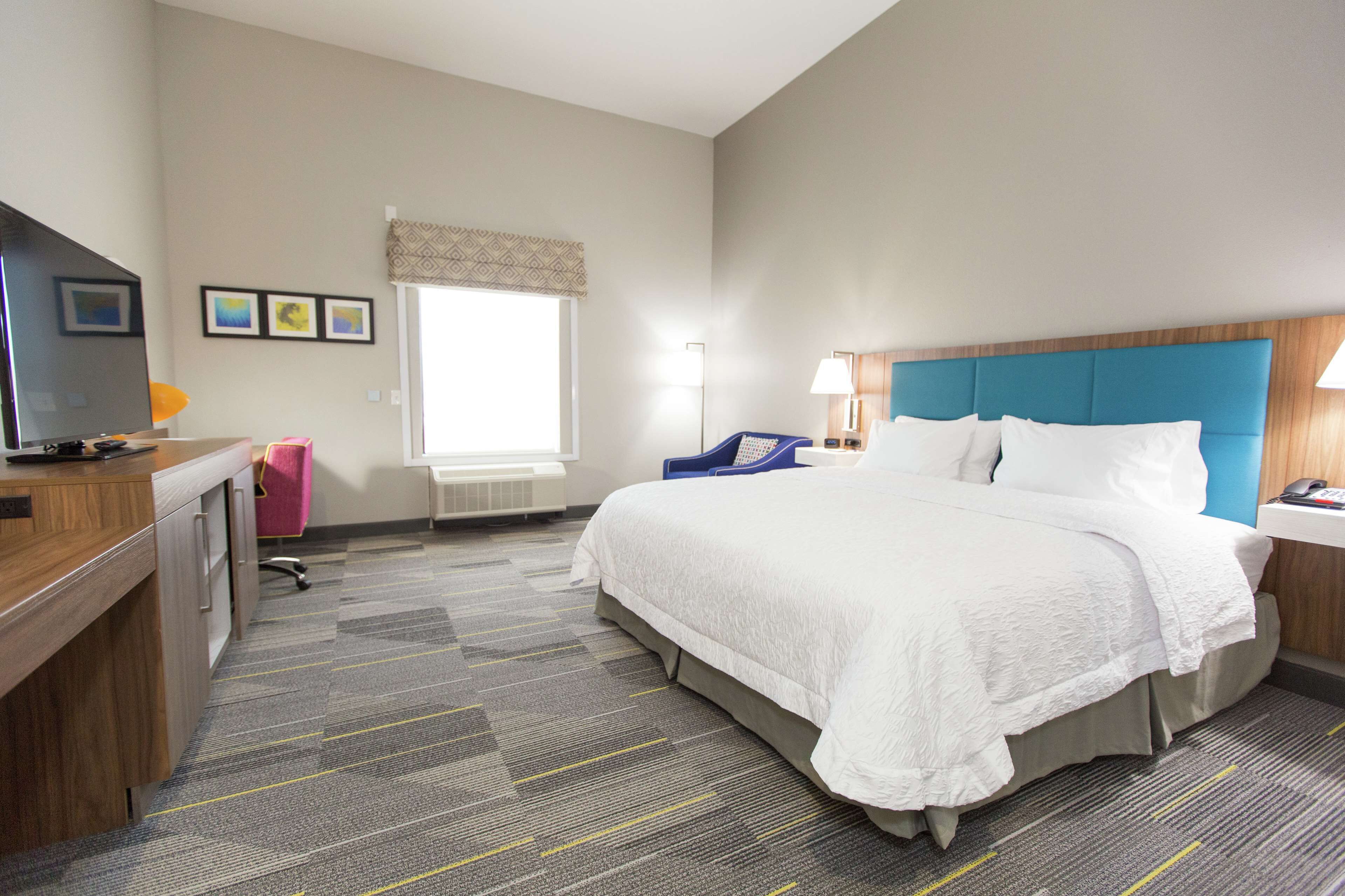 A hotel room with a bed, desk, chair, and a television.