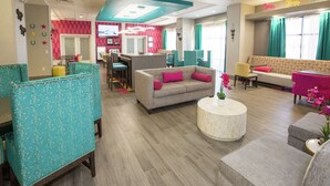 Un hall de hotel con zonas de estar, un mostrador de recepción y una pantalla de televisión.