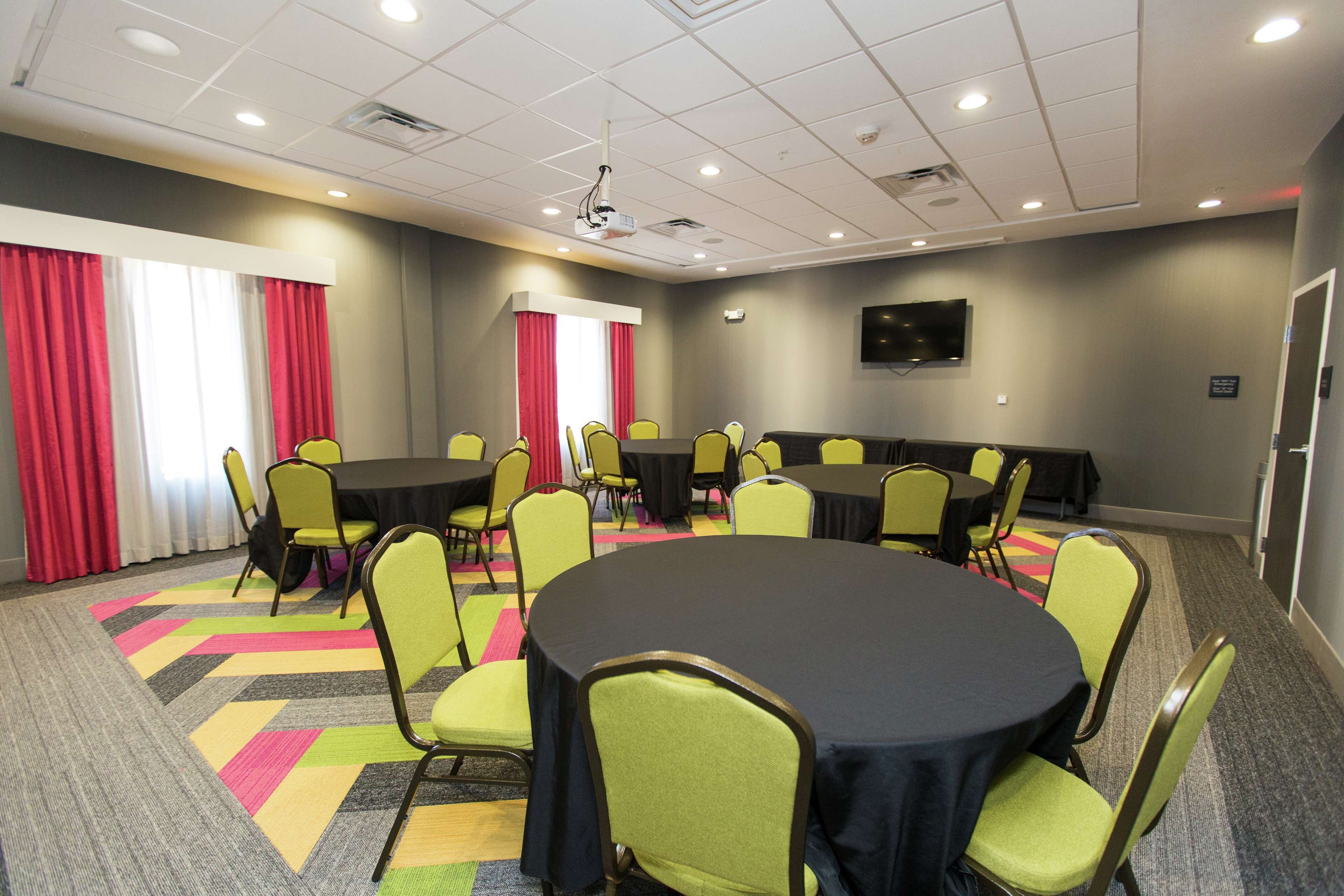 A conference room with round tables and chairs, a projector, and a television on the wall.