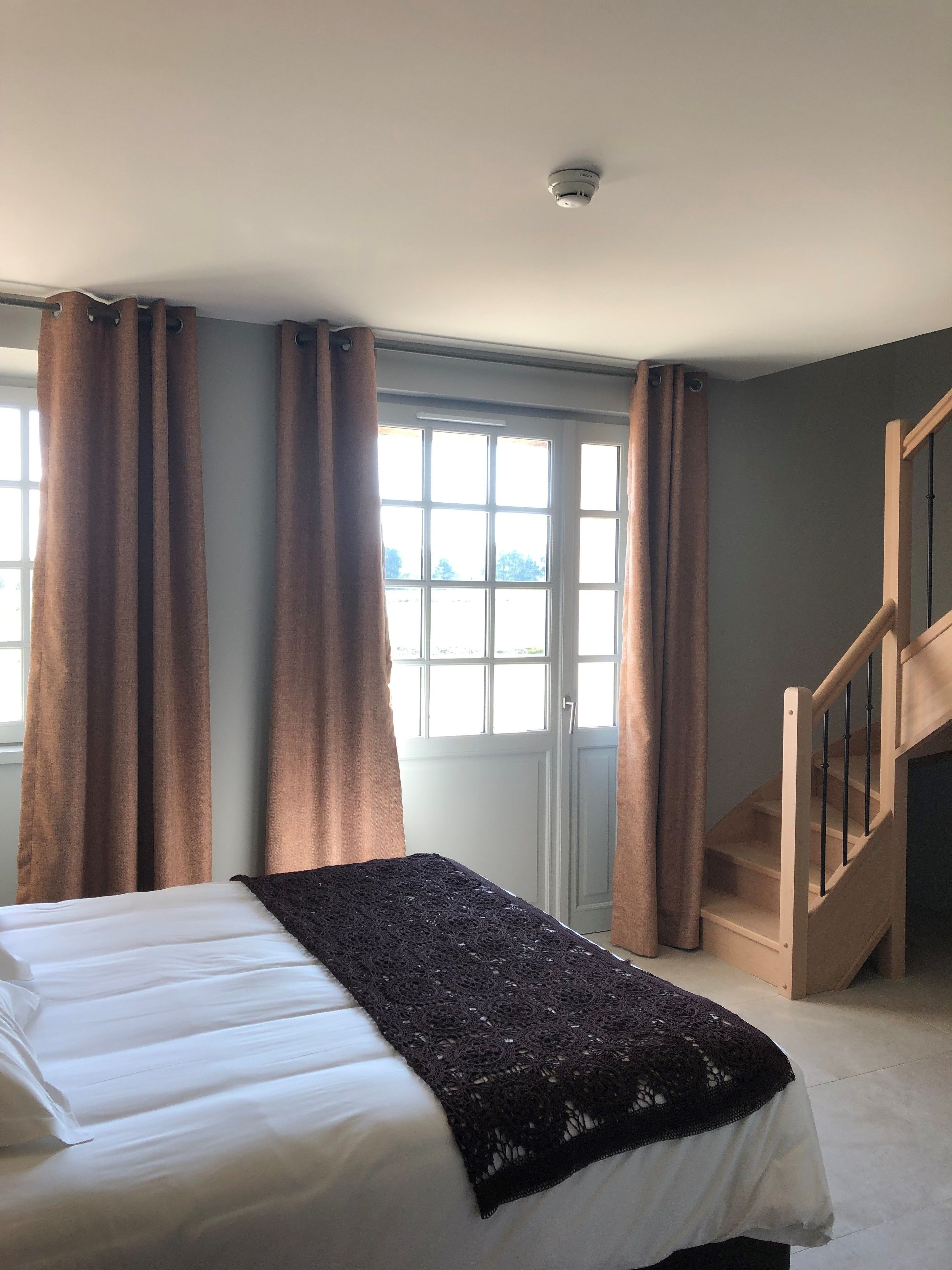 Quarto com cama, janela com cortinas, escada e detector de fumaça.