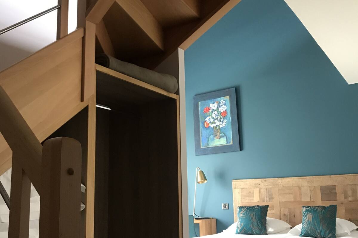 Een slaapkamer met een houten hoofdeinde, een bed met witte beddengoed en een blauwe muur met een schilderij.