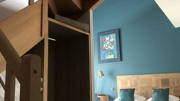 A bedroom with a wooden headboard, a bed with white bedding, and a blue wall with a painting.