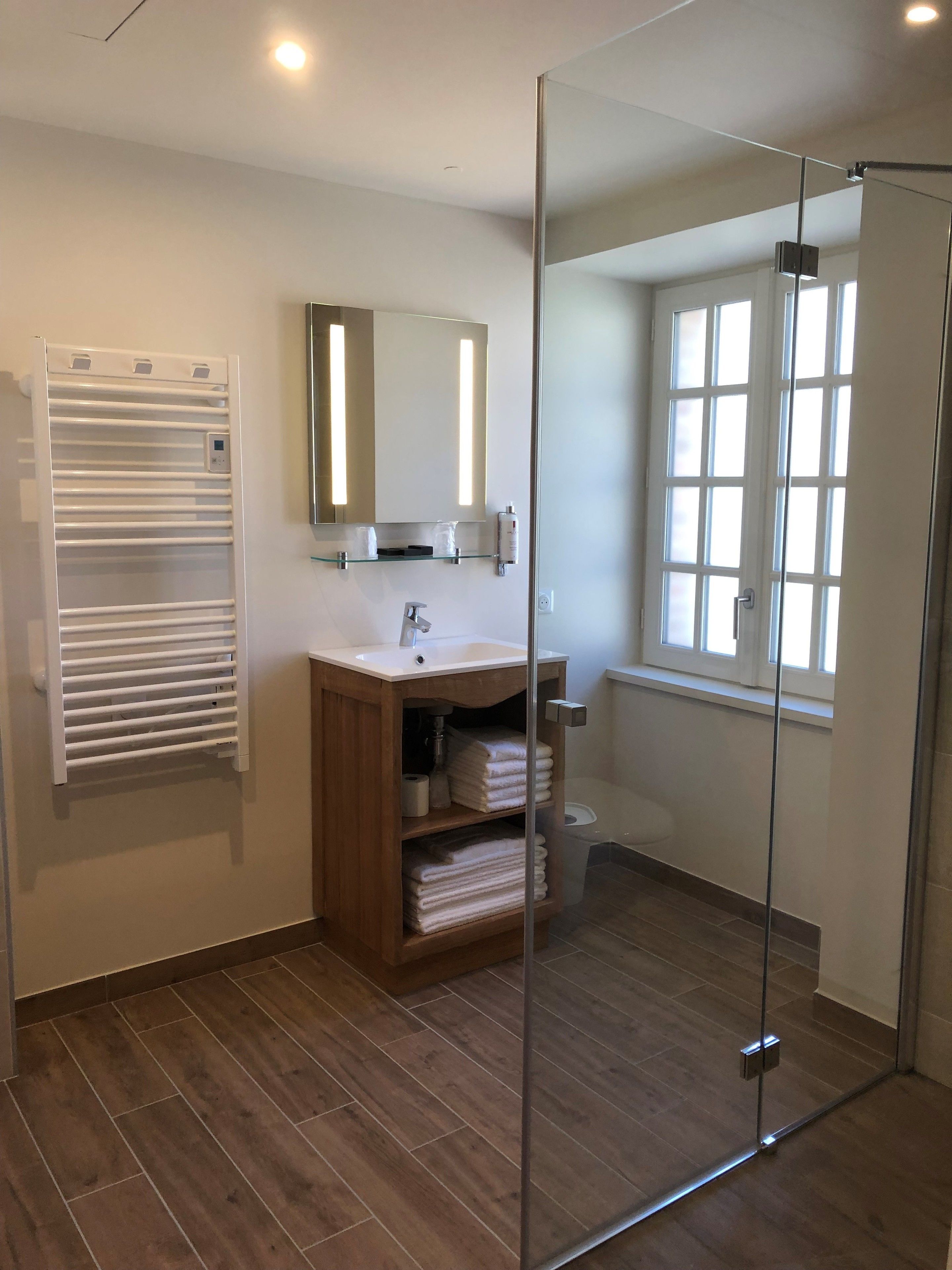 A modern bathroom with a glass shower enclosure, a wooden vanity, a white sink, and a built-in towel rack.
