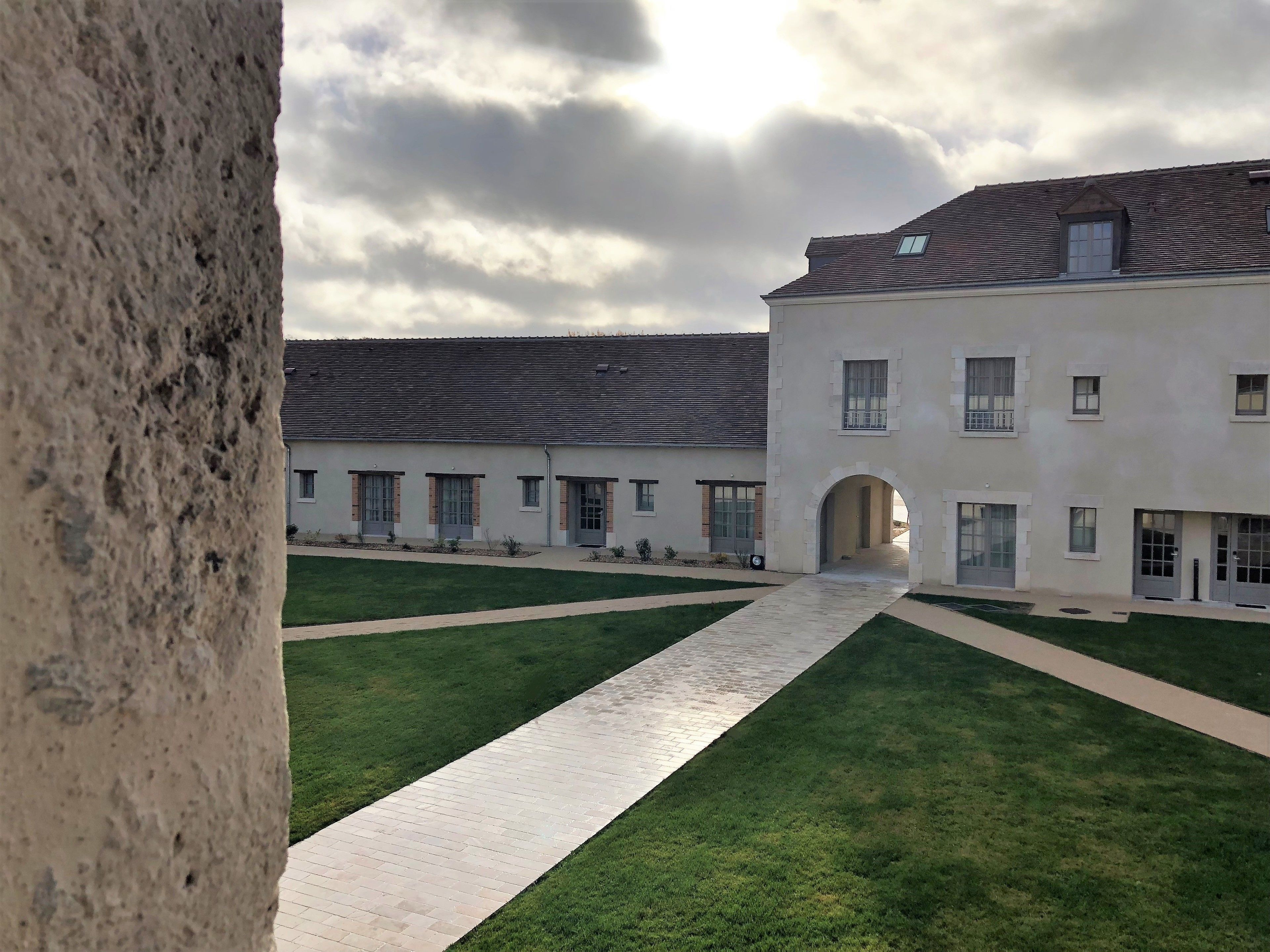 A courtyard with a paved walkway leading to a building with multiple windows and an arched entrance.