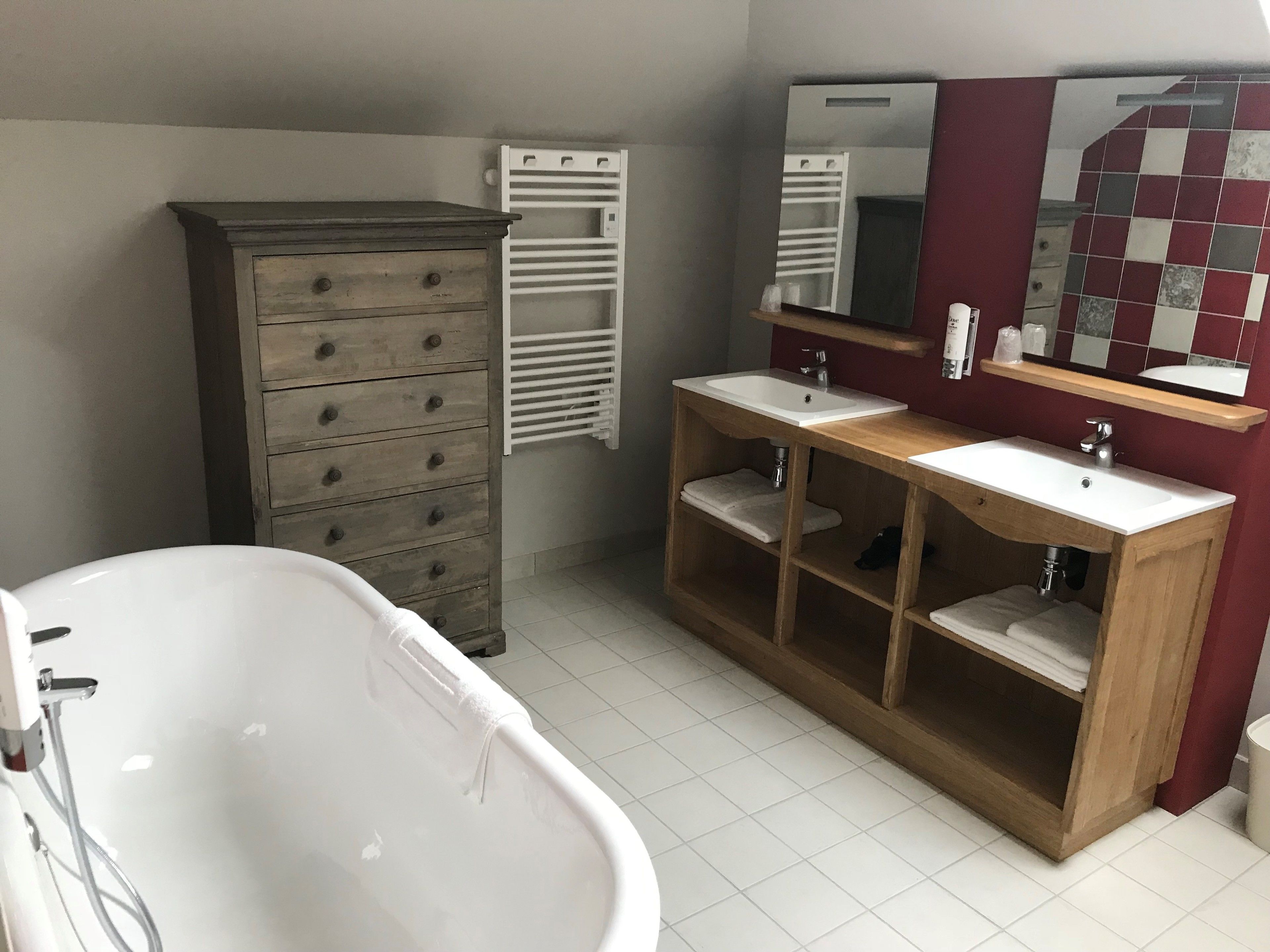 Een badkamer met een badkuip, een houten wastafelmeubel met twee wastafels, een spiegel en een handdoekhouder.